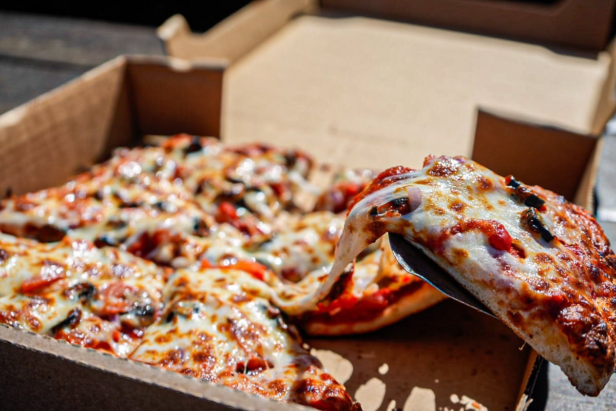 Pizza slices in cardboard boxes with melted cheese and toppings, one slice pulled out to the side