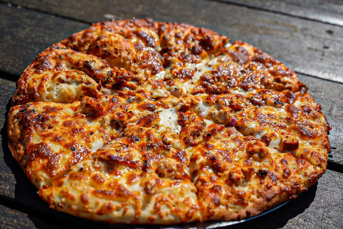 Whole pizza with melted cheese and toppings on a wooden surface