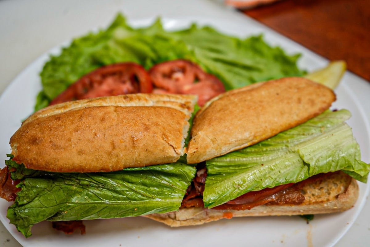 A fresh sandwich on a white plate filled with crisp lettuce, sliced tomatoes, and other fillings