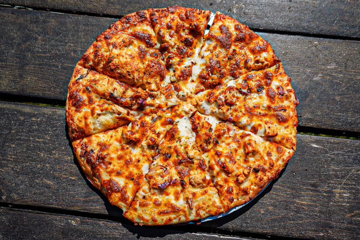 Whole pepperoni pizza with melted cheese on dark wooden surface, sliced into eight portions