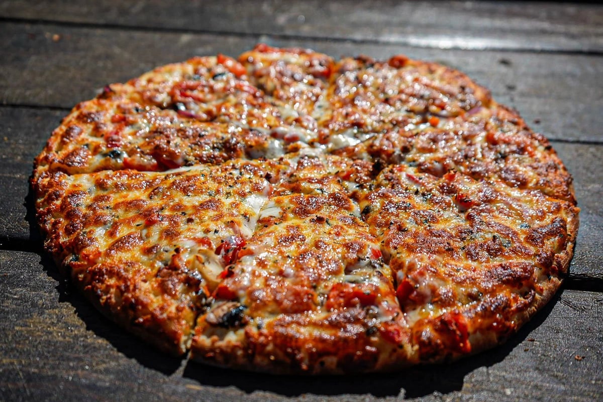 A golden-brown pizza with melted cheese and toppings on a dark wooden surface, cut into slices