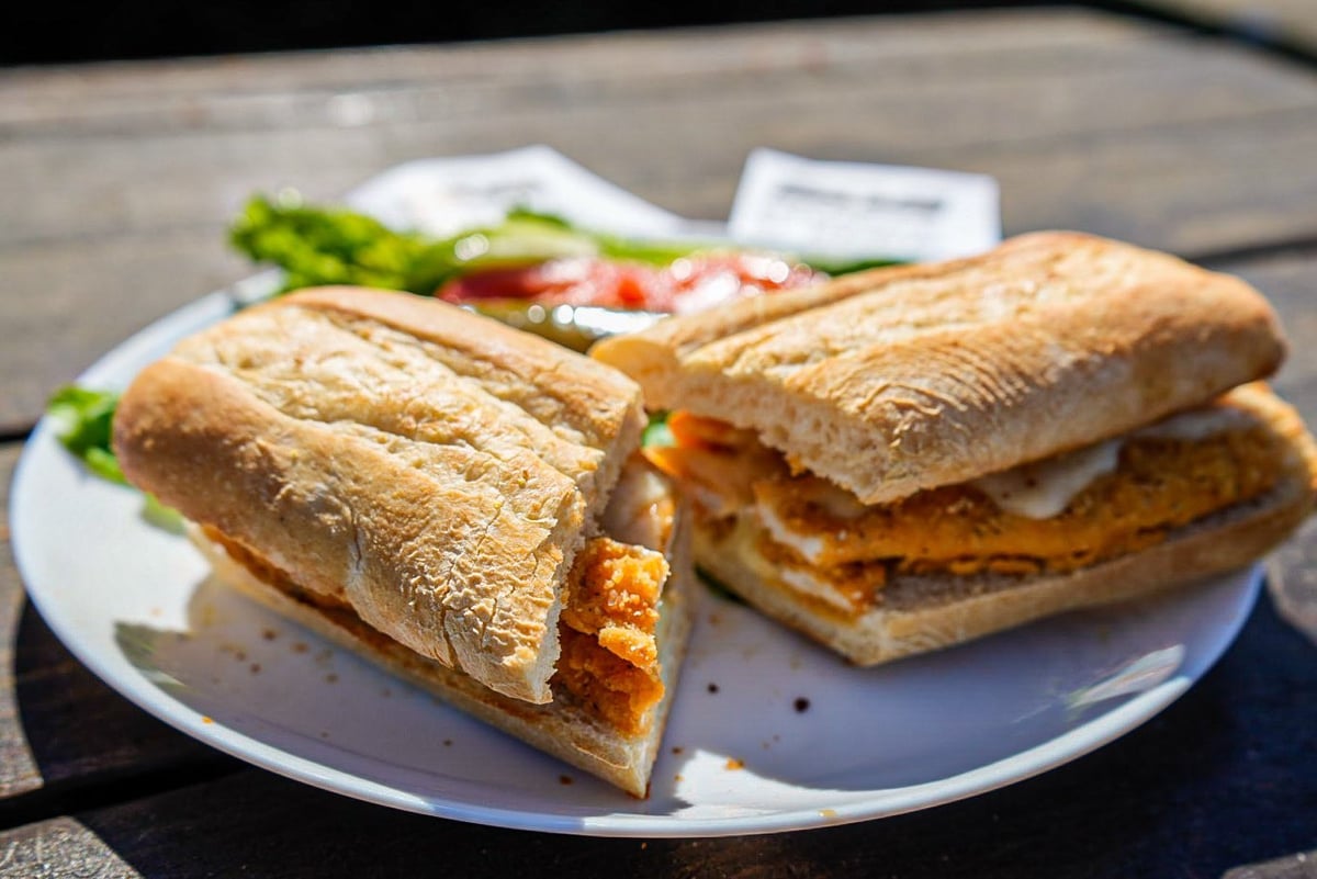 Two toasted sandwiches with melted cheese and vegetables on a white plate outdoors