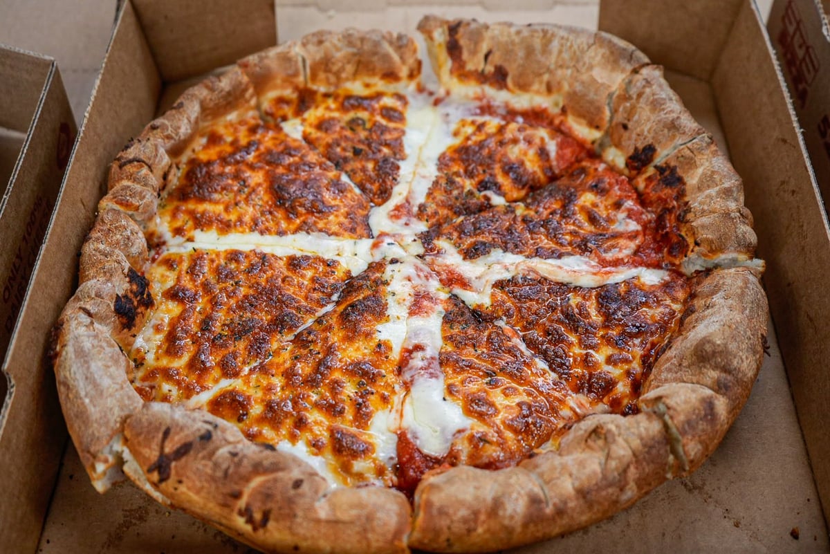 Pepperoni pizza in cardboard box with thick crust and melted cheese, cut into slices
