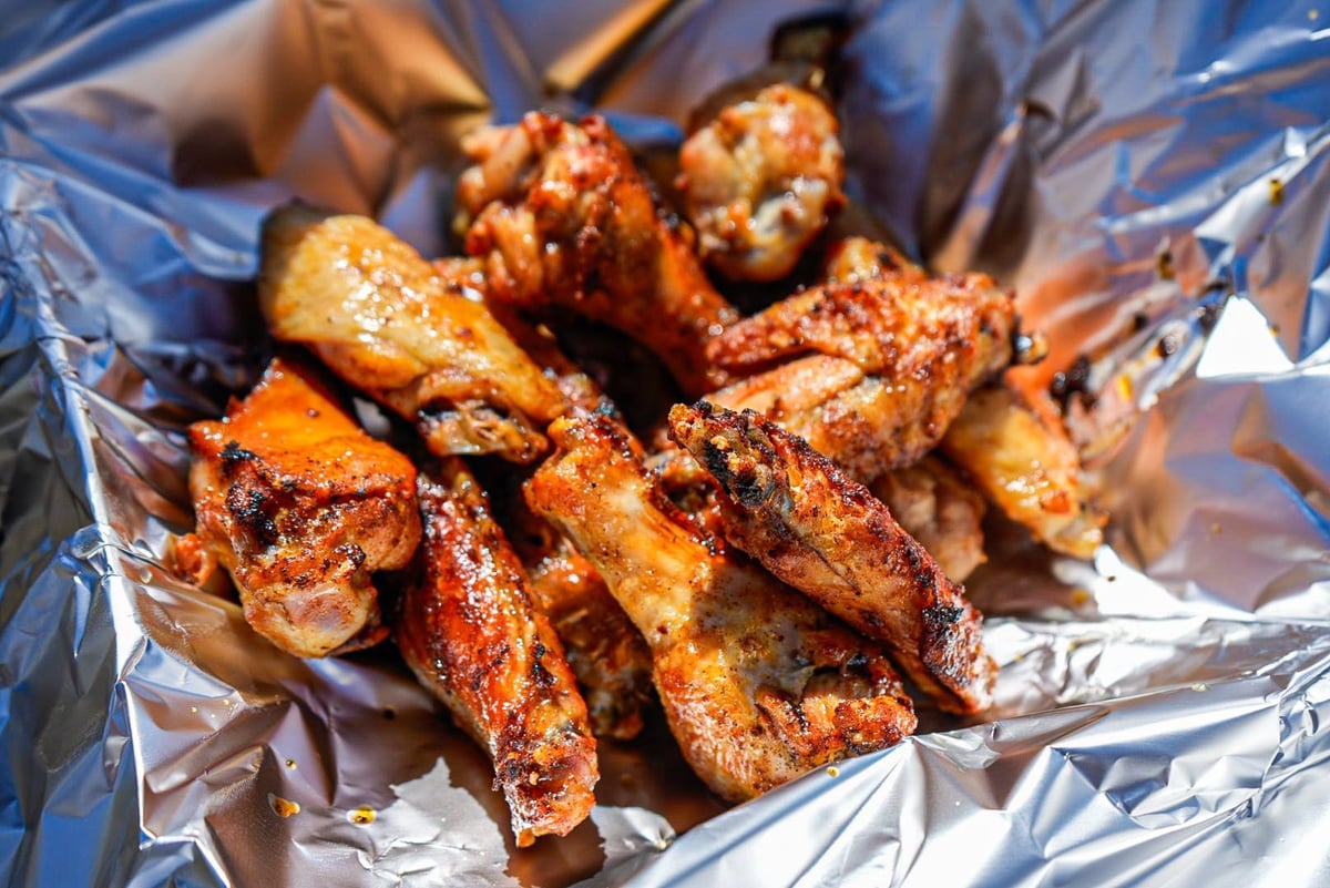 Golden-brown seasoned chicken pieces arranged on aluminum foil with visible spice coating and charred edges