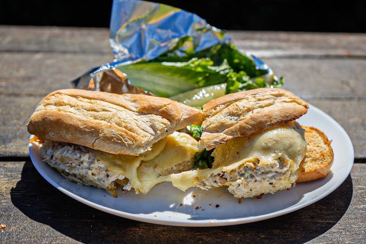 Croissant sandwich with melted cheese and herbs on a white plate with salad in the background